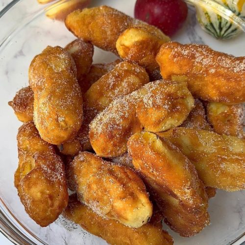 A bowl of golden brown apple doughnuts generously coated with a delightful mix of cinnamon and sugar.