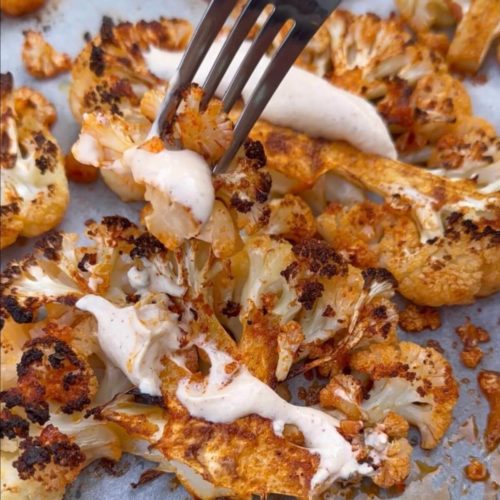 Roasted Cauliflower Steaks with Creamy Tahini Sauce, garnished with fresh herbs and sesame seeds on a white plate.