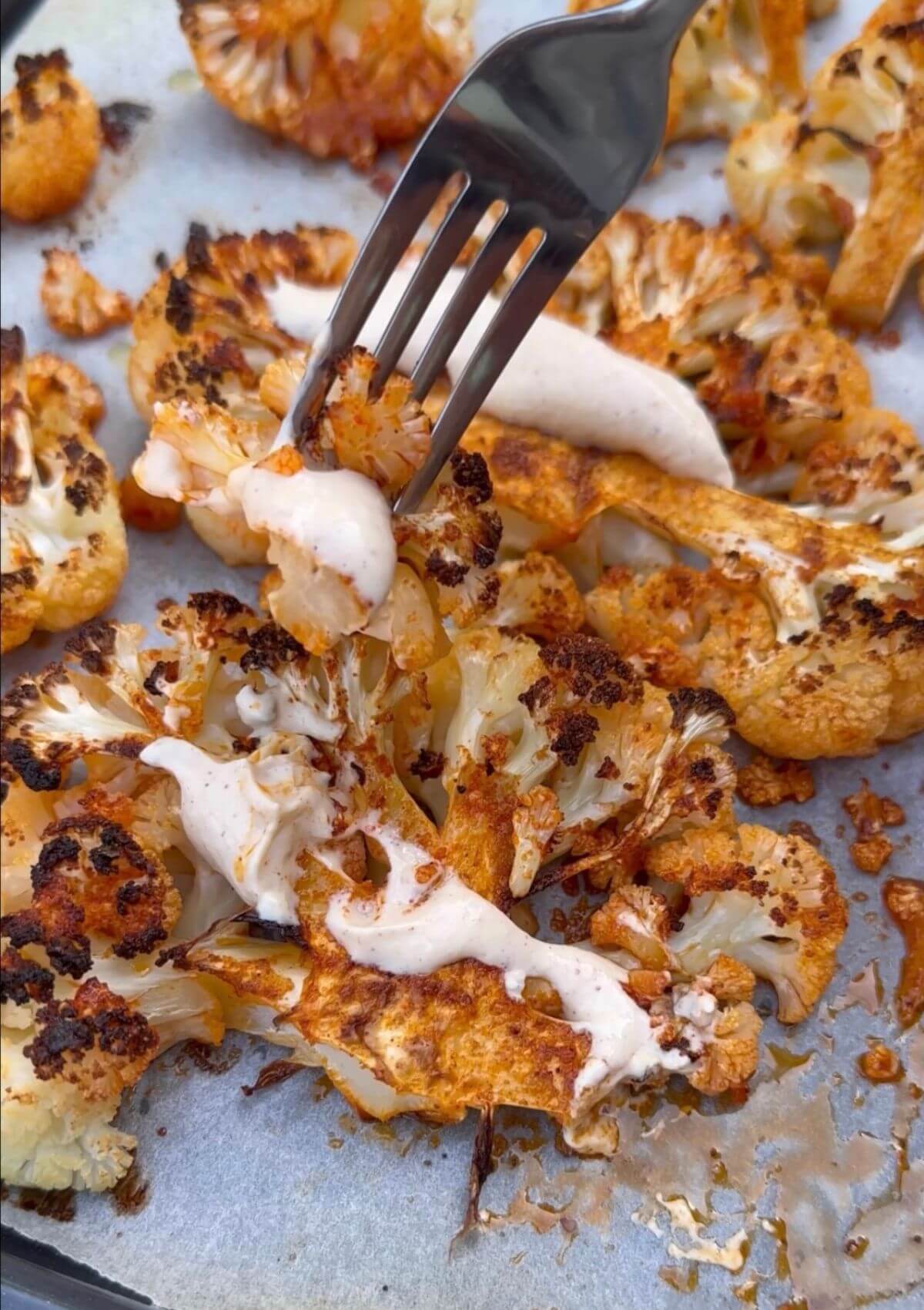 Roasted Cauliflower Steaks with Creamy Tahini Sauce, garnished with fresh herbs and sesame seeds on a white plate.
