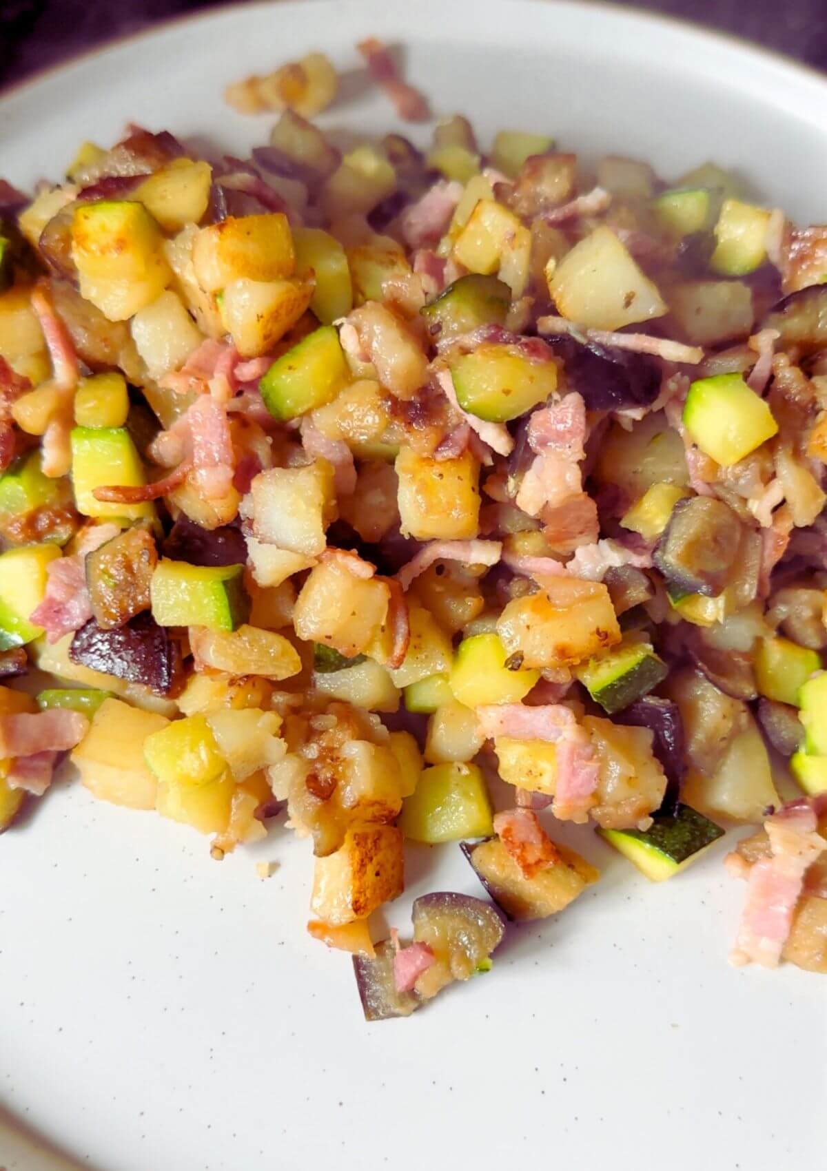 Plate of sizzling bacon, tender potatoes, and sautéed zucchini stir-fry