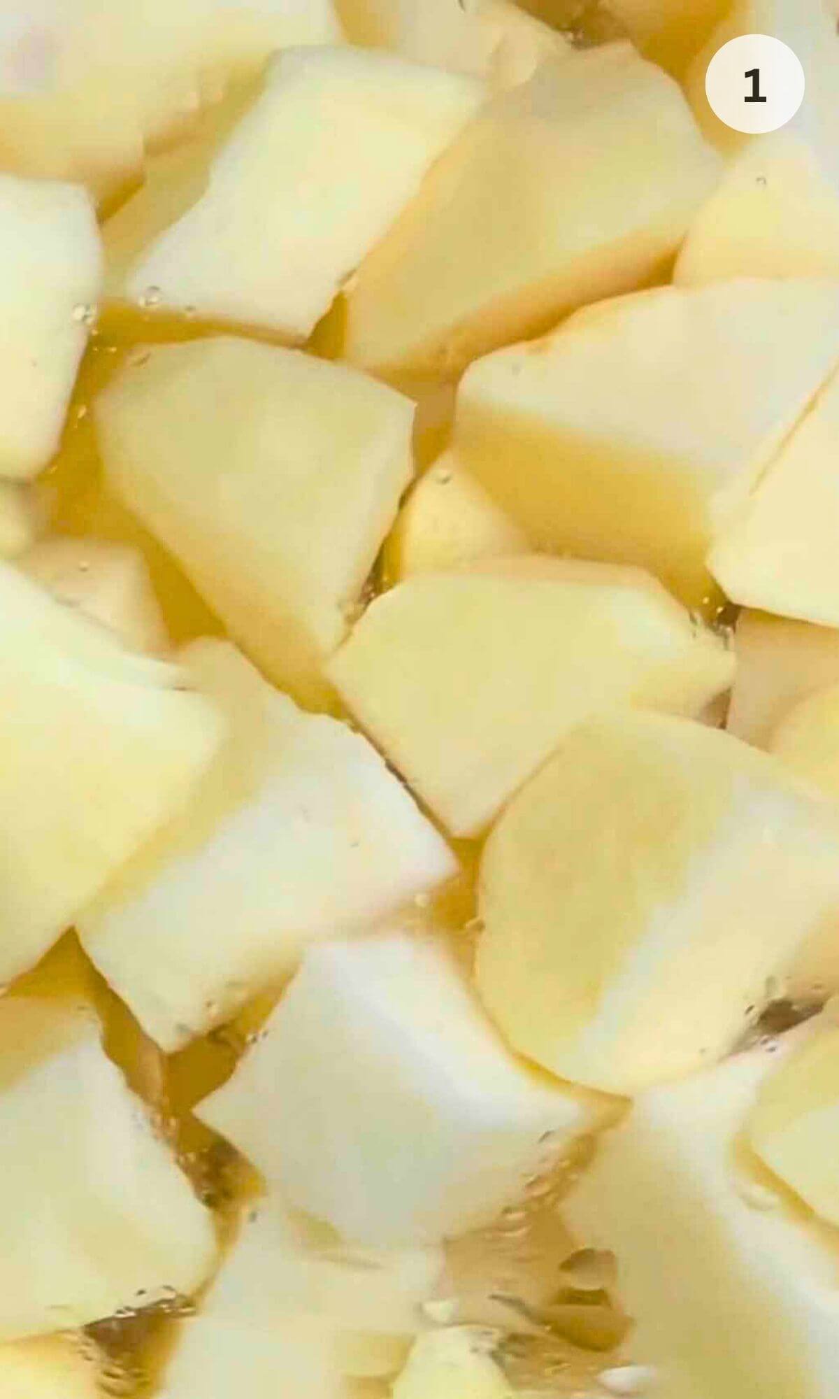 A photo showing raw diced white potatoes in a pan of water, prepared for boiling.