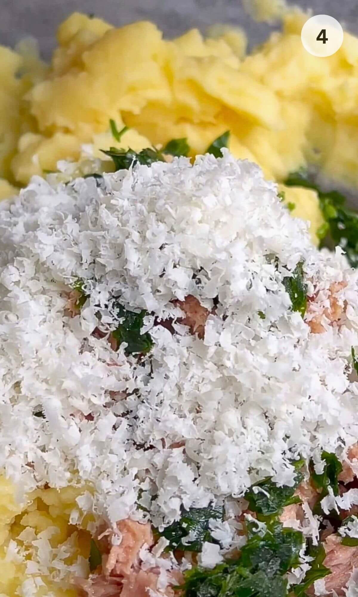 Mashed potatoes, canned tuna, chopped parsley, grated parmesan in a bowl ready to be mixed.