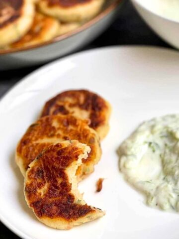 A photo showing a plate with fried potato and tuna patties served with tzatziki sauce.