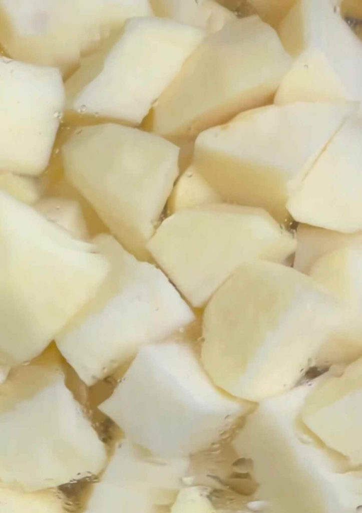 A photo showing raw diced white potatoes in a pan of water, prepared for boiling.