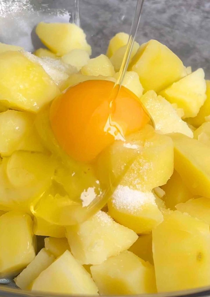 Diced white potatoes in a bowl, accompanied by a raw egg for mashing.