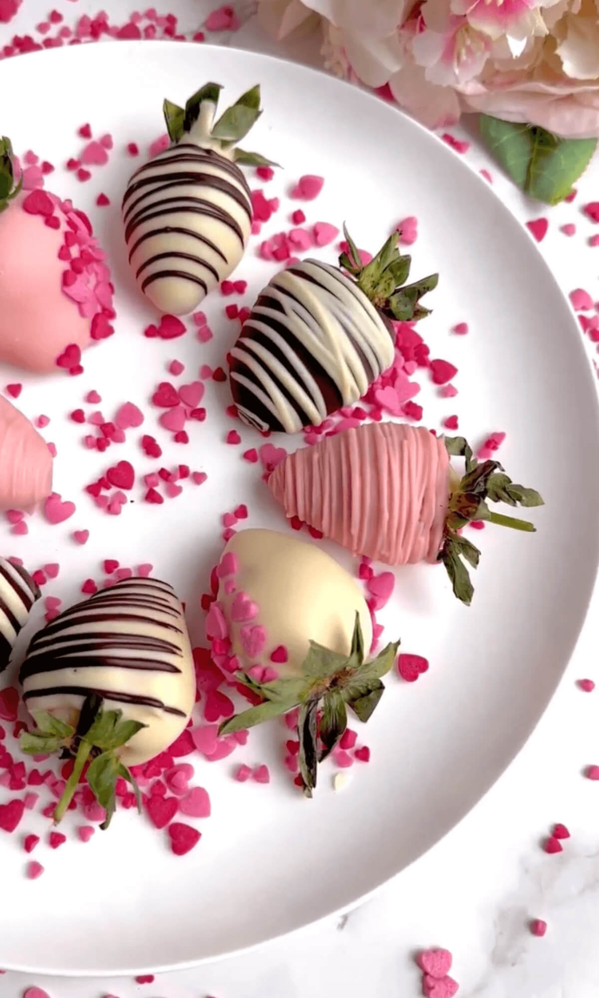 Colorful strawberries dipped in chocolate. Some are pink, red, or white, while others have dark chocolate. Each berry is decorated with striped chocolate designs, making them look delicious and pretty.