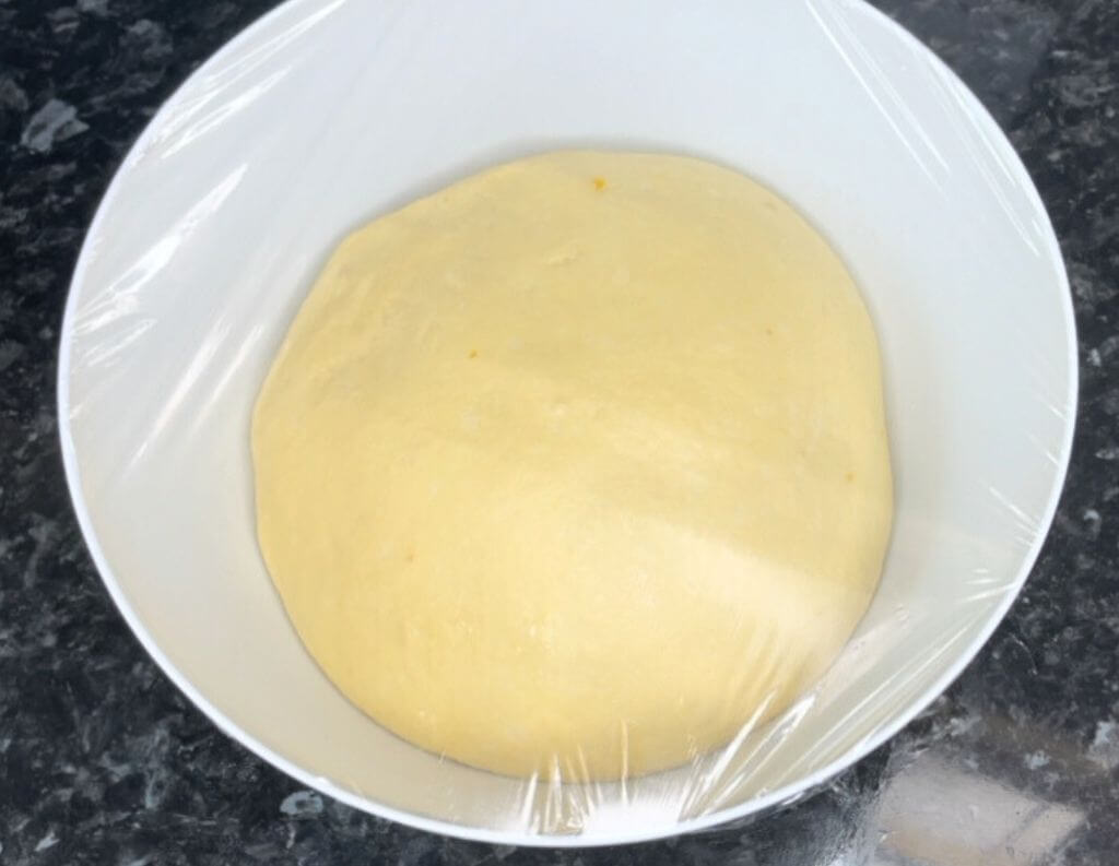 Picture of walnut roll dough rising in a bowl, covered with plastic wrap