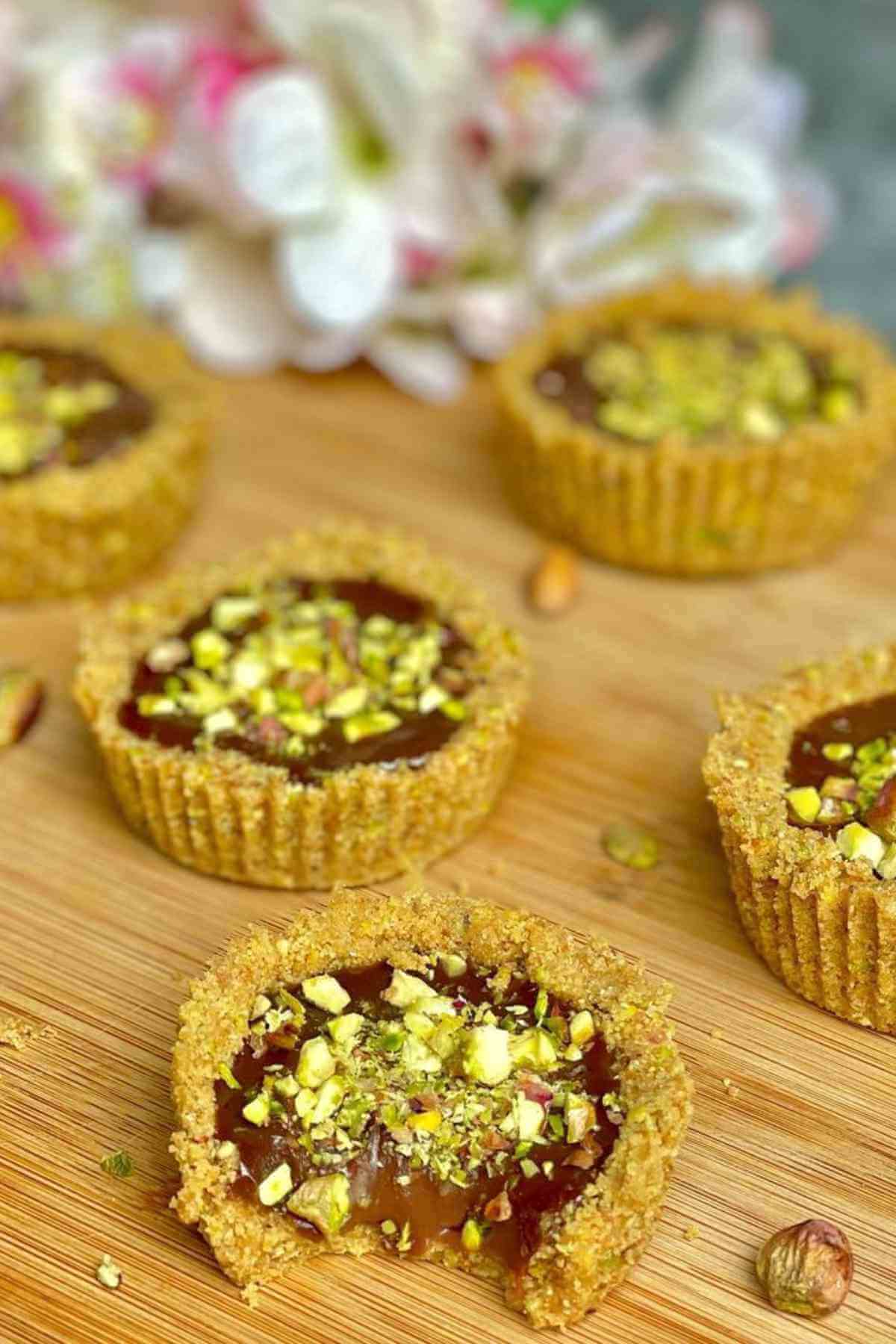 Chocolate Mini Tarts garnished with chopped pistachios on a wooden board. 