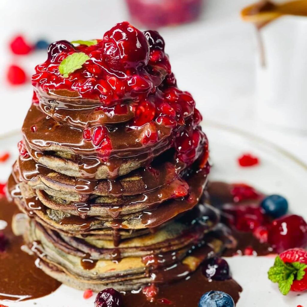 Stack of American-style Berry Pancakes drizzled with berry sauce and chocolate ganache