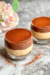 Chocolate and Caramel Pudding in two glasses, one half filled with chocolate pudding and the other half with caramel pudding, topped with cocoa powder