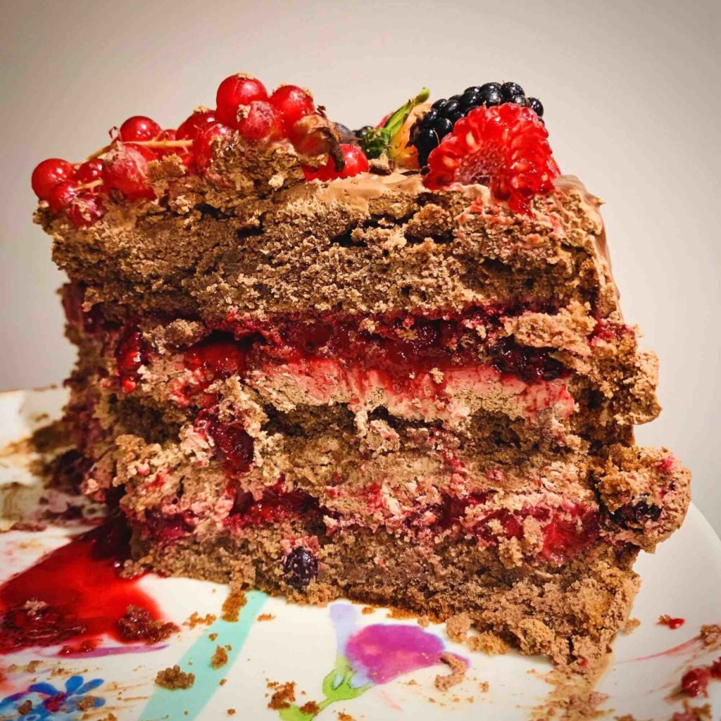 A slice of chocolate cake topped with fresh berries and a rich chocolate drizzle. The section shows 3 layers of sponge cake, 2 layers of chocolate mousse and 2 layers of berry sauce. 