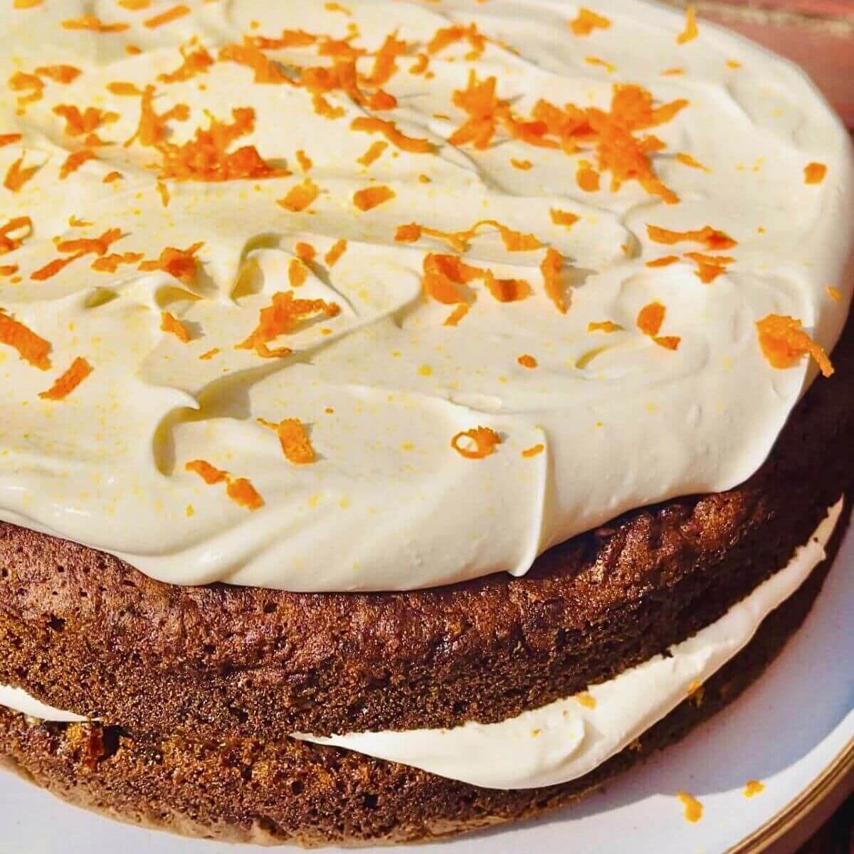 A whole super moist carrot cake with cream cheese frosting on a cake platter.