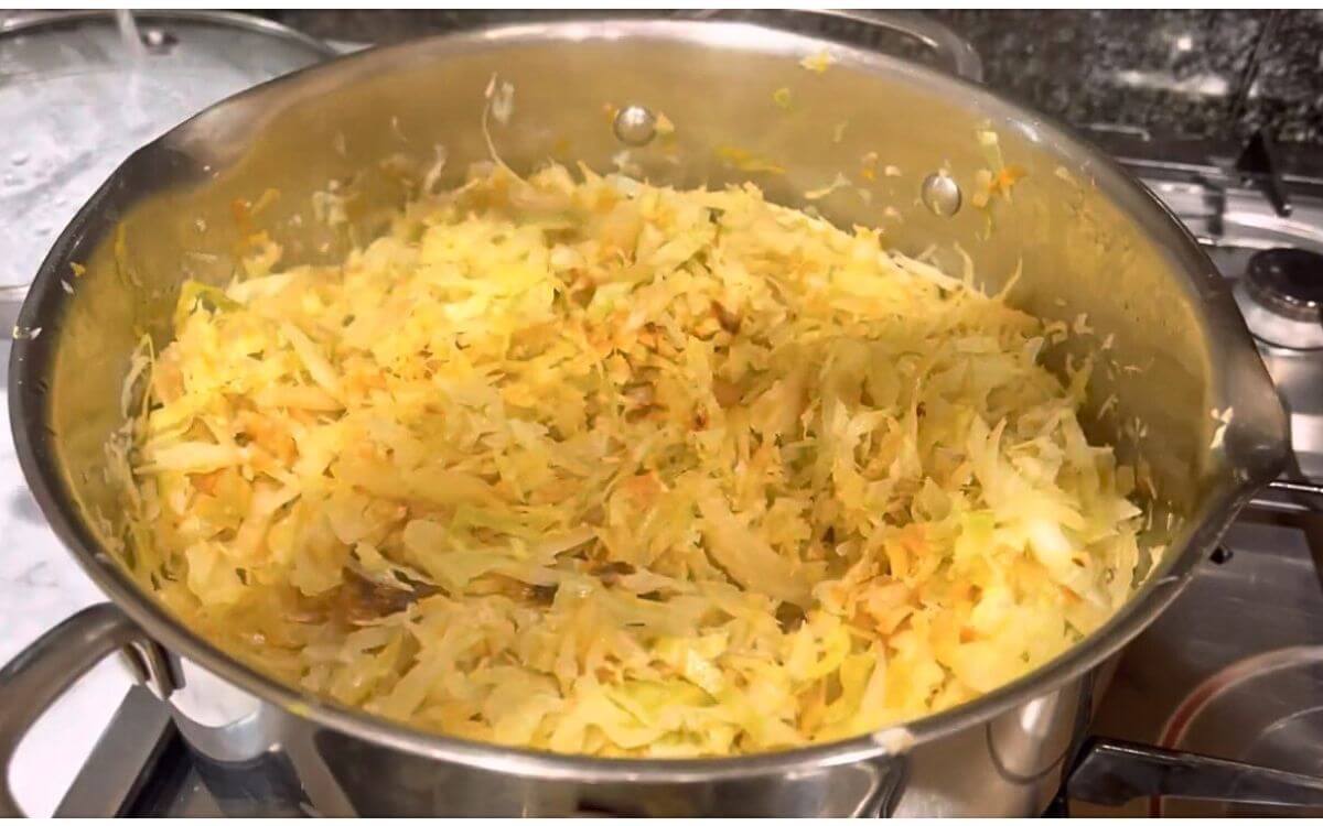 Cabbage cooking in covered pan over low-medium heat, reducing to about half its original volume.