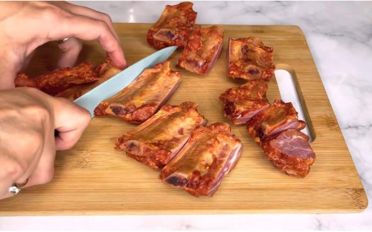 Smoked pork ribs and chopped cabbage arranged separately on a cutting board, ready for cooking.