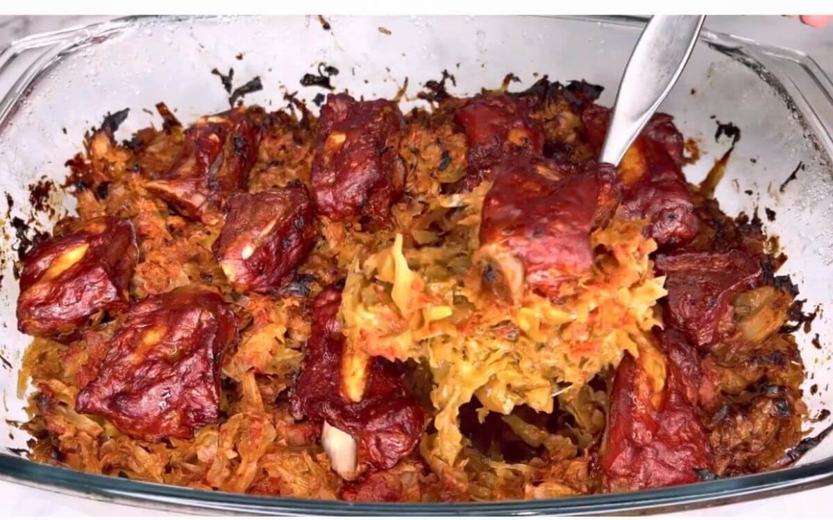 Smoked pork ribs and cabbage casserole in a baking dish, with a spoonful lifted in the air.