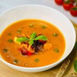Creamy Roasted Vegetable Soup in a bowl garnished wit pesto and roasted veggies and fresh basil.