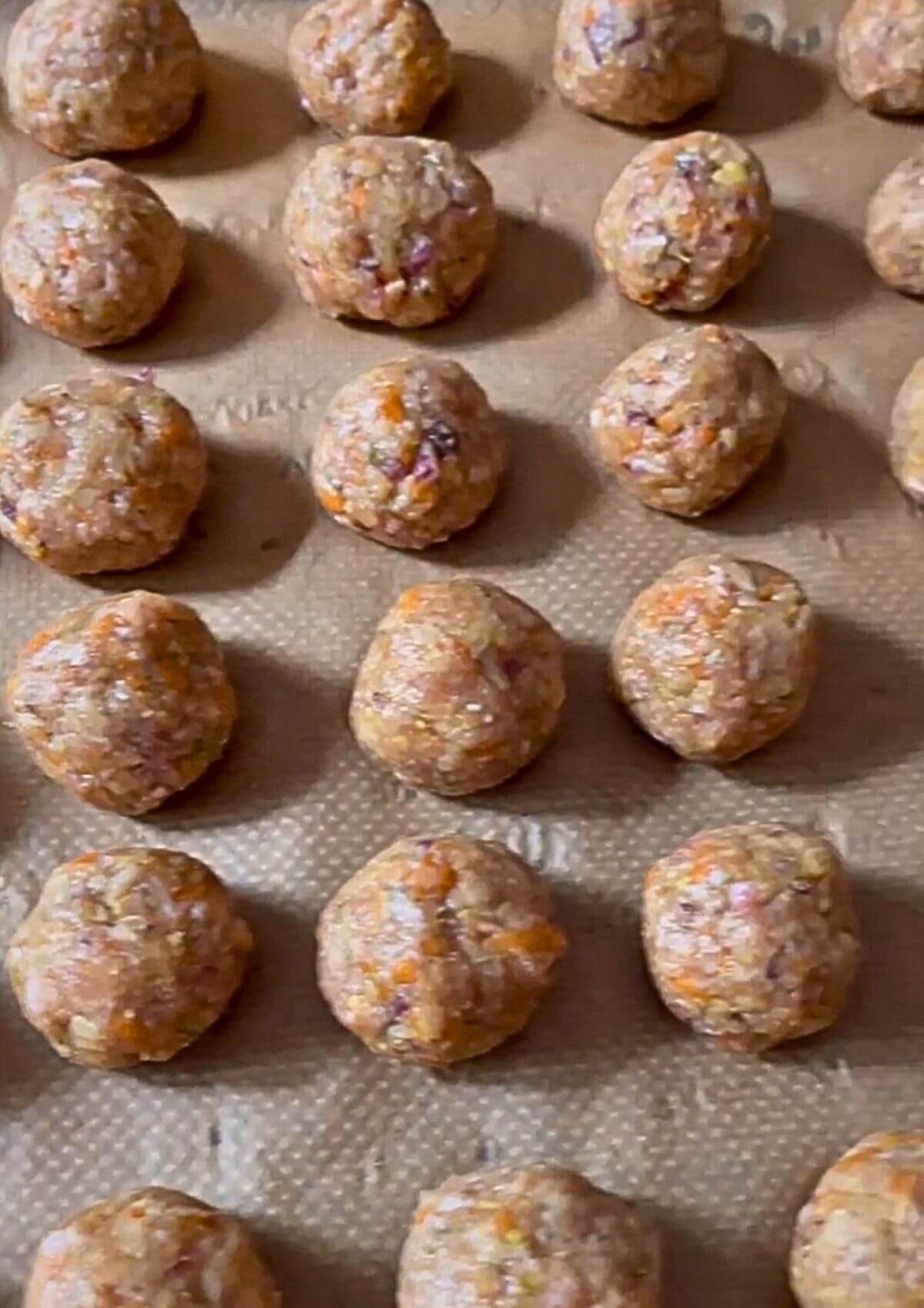 Shaped meatballs placed on a baking sheet, spaced apart, with hands dipped in water for easier rolling.