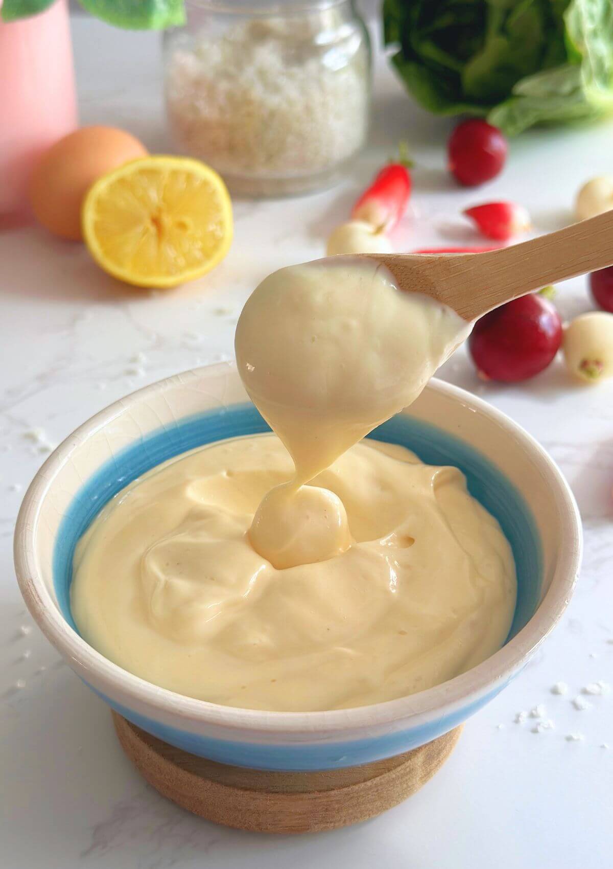 Homemade 4-ingredient mayo in a bowl, scooped with a wooden spoon to show creamy texture.