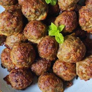 Baked meatballs in a ceramic white bowl decorated with mint leaves.