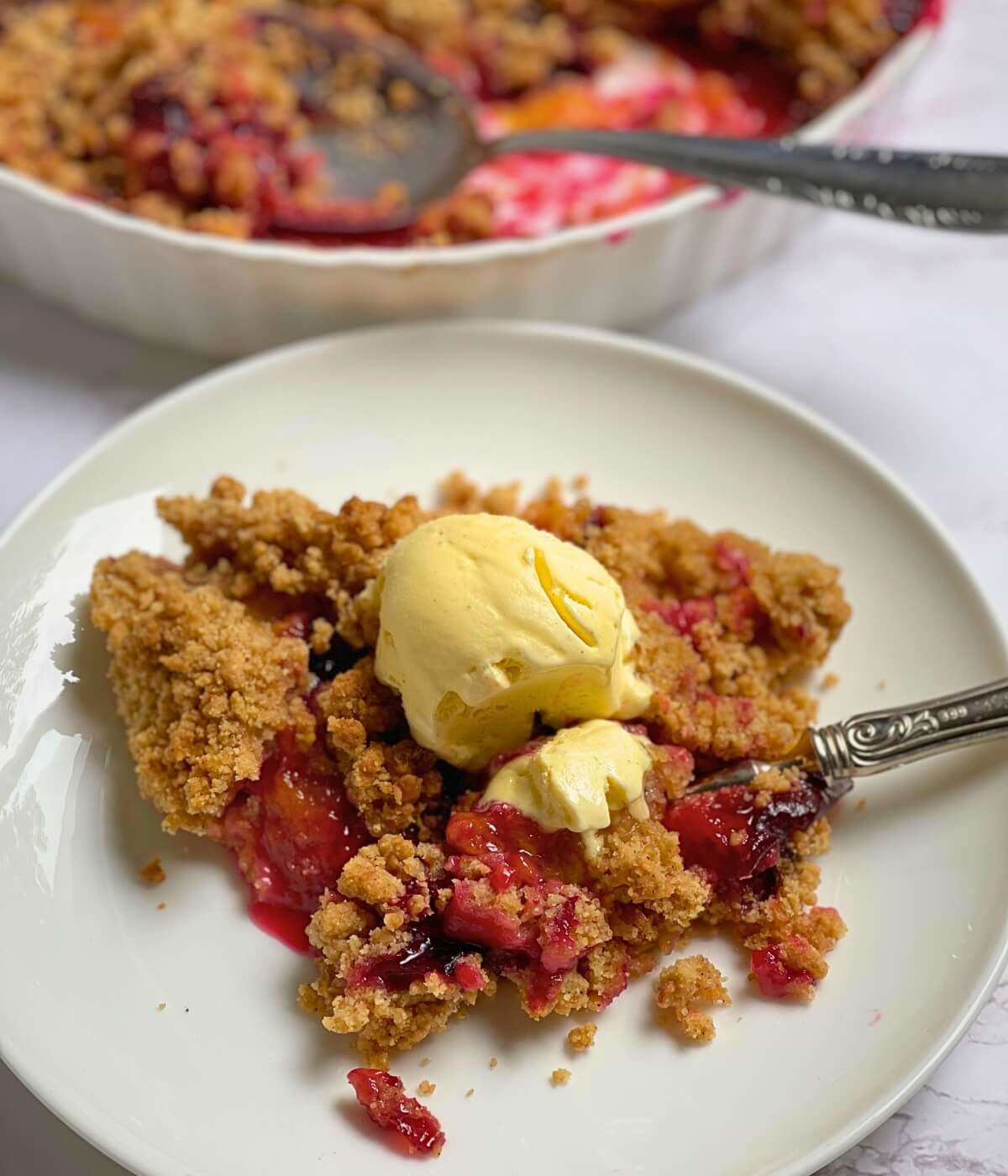 Plum crumble on a plate with vanilla ice cream scoops on top.