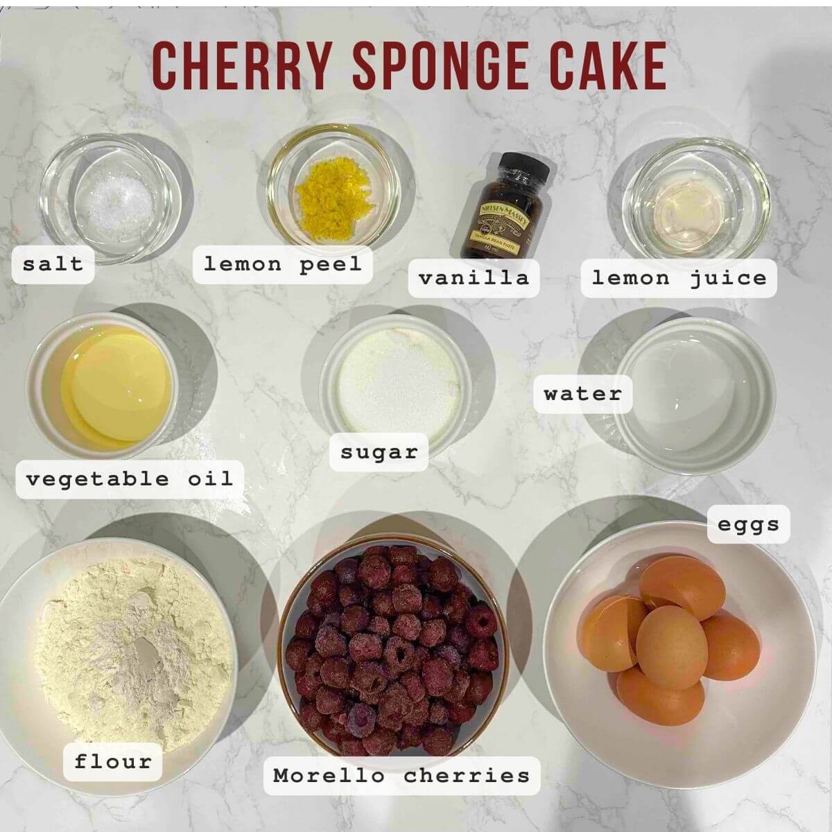 Ingredients for sponge cake laid out, including eggs, cold water, salt, vinegar or lemon juice, sugar, bourbon vanilla sugar, flour, oil, grated lemon zest, pitted cherries, and optional vanilla powdered sugar for dusting.