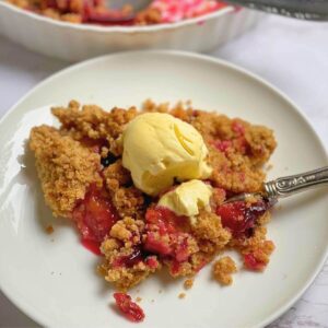 Plum crumble on a plate with a scoop of vanilla ice cream.