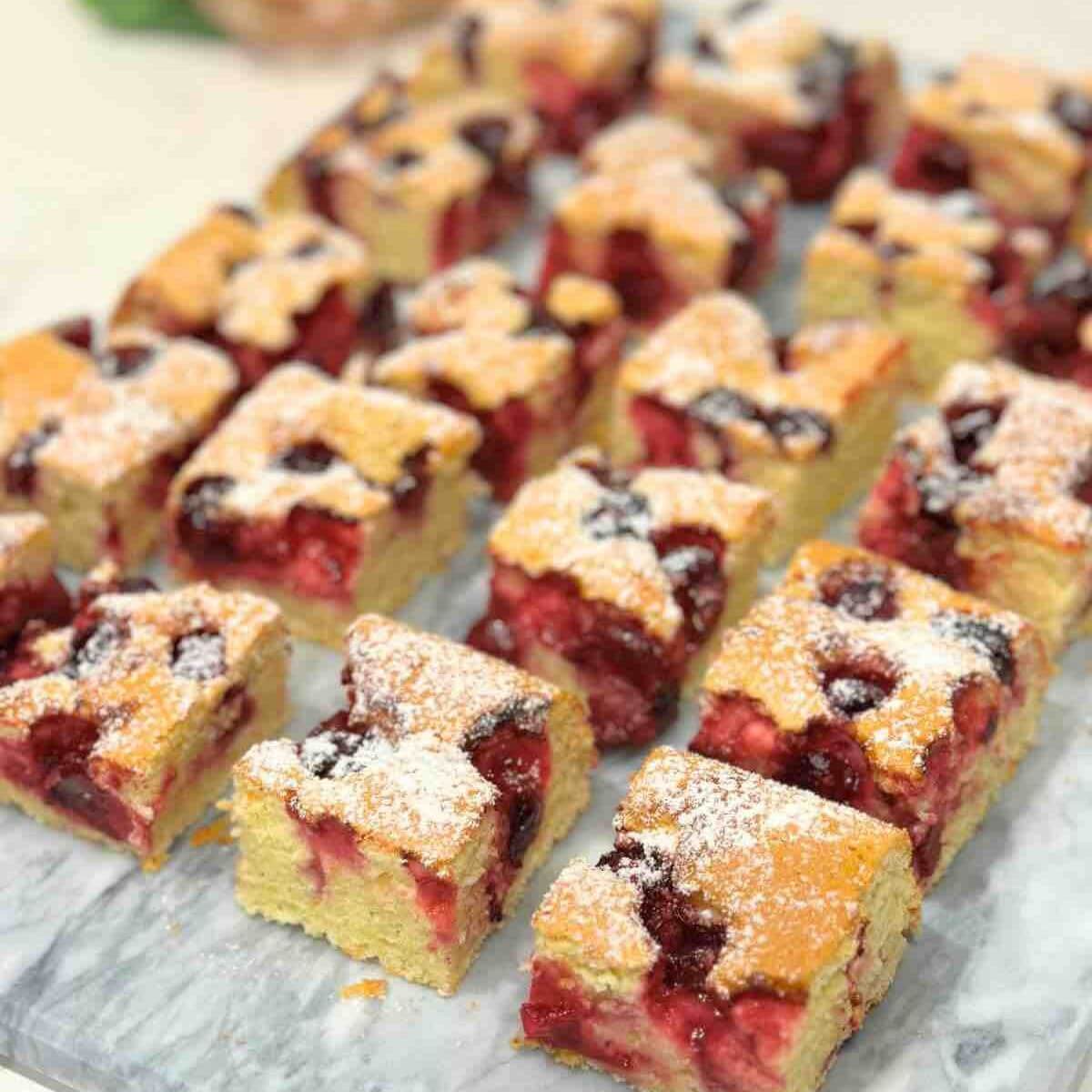 Squares of Morello Cherry Sponge Cake displayed on a marble surface, showcasing the moist center filled with juicy cherries.