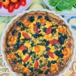 Easy spinach cherry tomato quiche in white ceramic dish with fresh leaves.