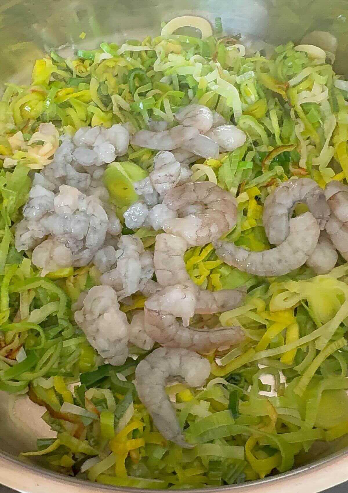 Pouring egg mixture over leeks and shrimp in pan. 