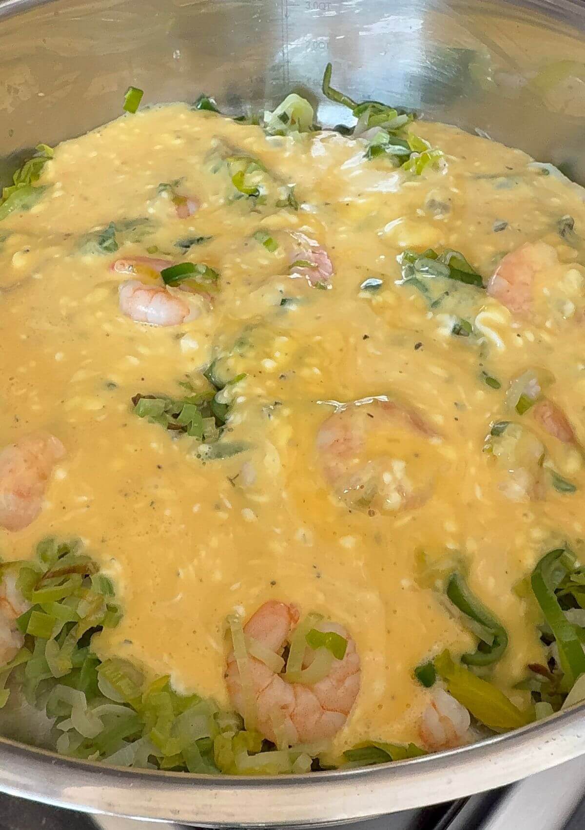 Pouring egg mixture over leeks and shrimp in pan.