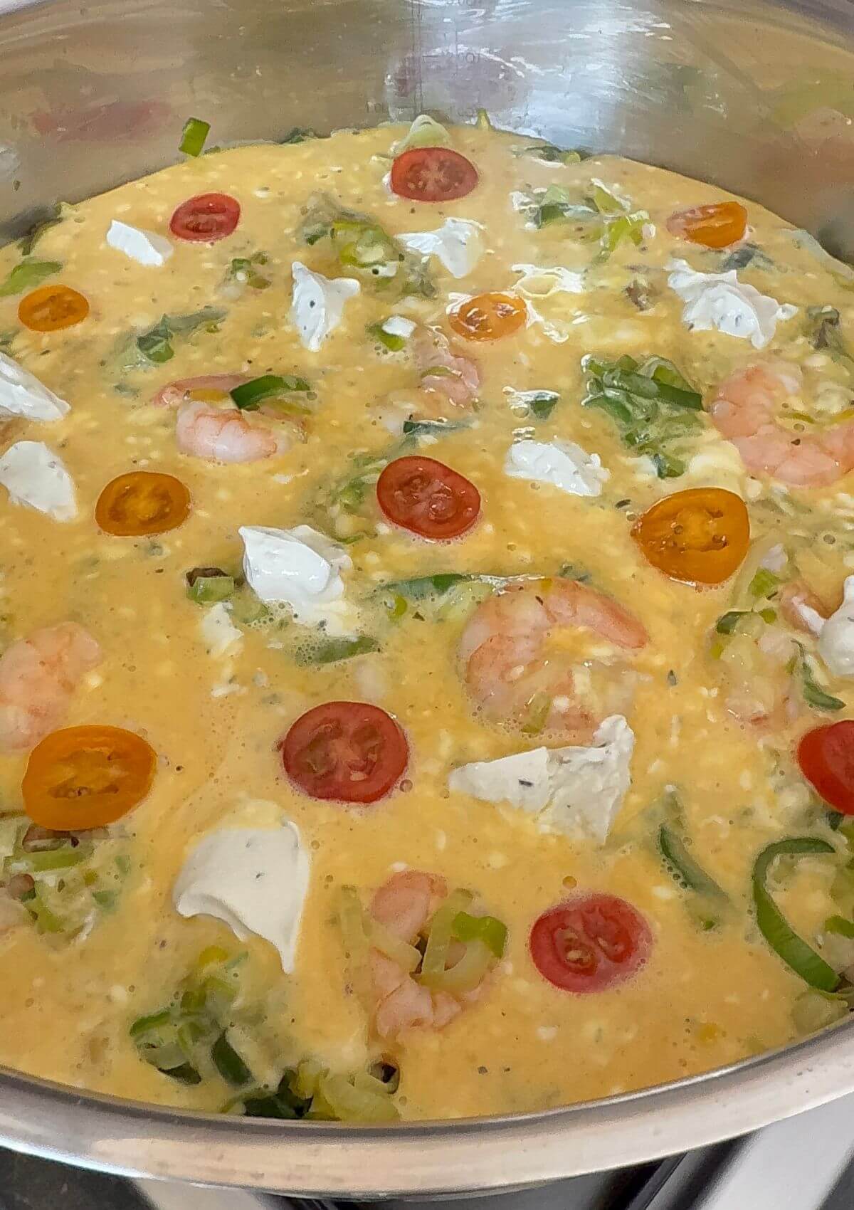 Unbaked shrimp frittata with leeks, tomato halves and cheese chunks.