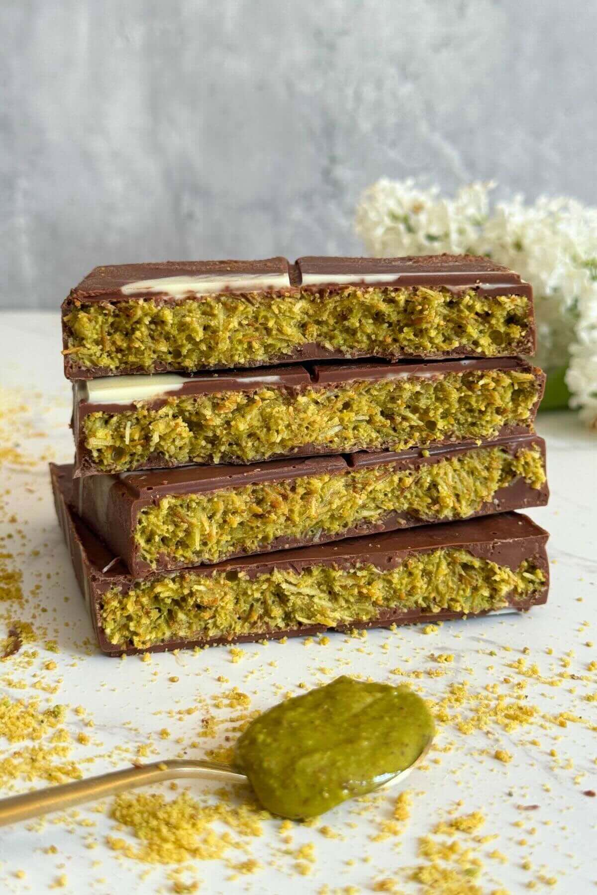 Chocolate bar broken into four pieces stacked to show pistachio, tahini, and kadaif filling.
