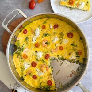 Shrimp and leek frittata in a stainless steel pan, one slice removed.