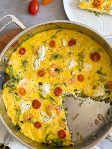 Shrimp and leek frittata in a stainless steel pan, one slice removed.