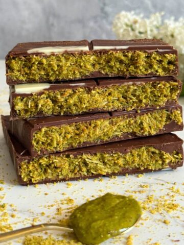 Chocolate bar broken into four pieces stacked to show pistachio, tahini, and kadaif filling.