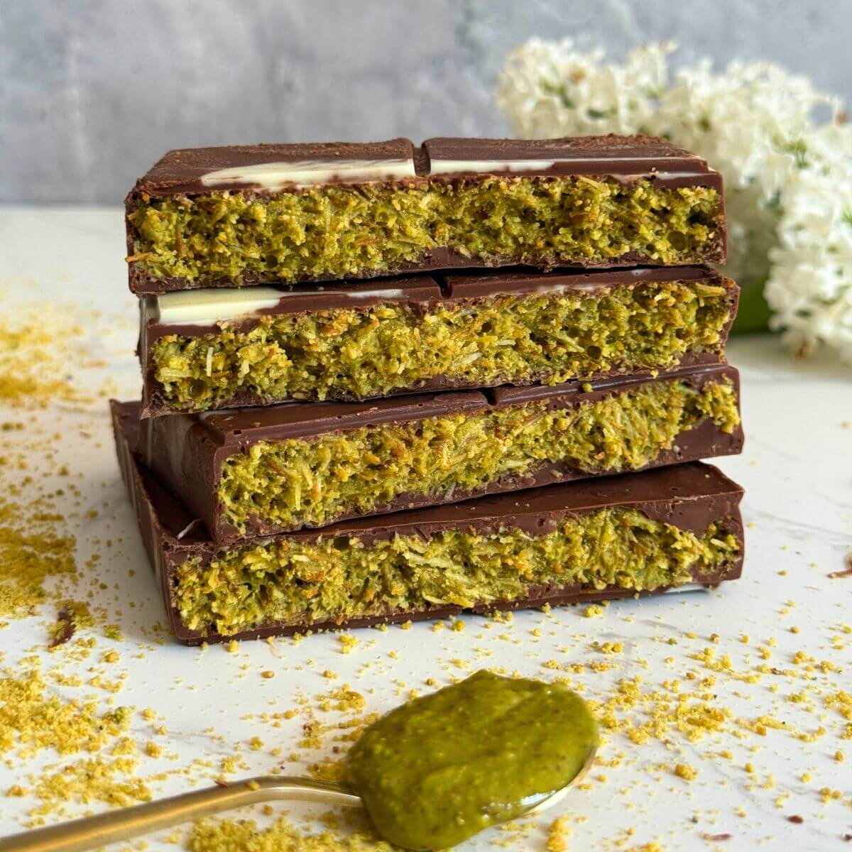Chocolate bar broken into four pieces stacked to show pistachio, tahini, and kadaif filling.