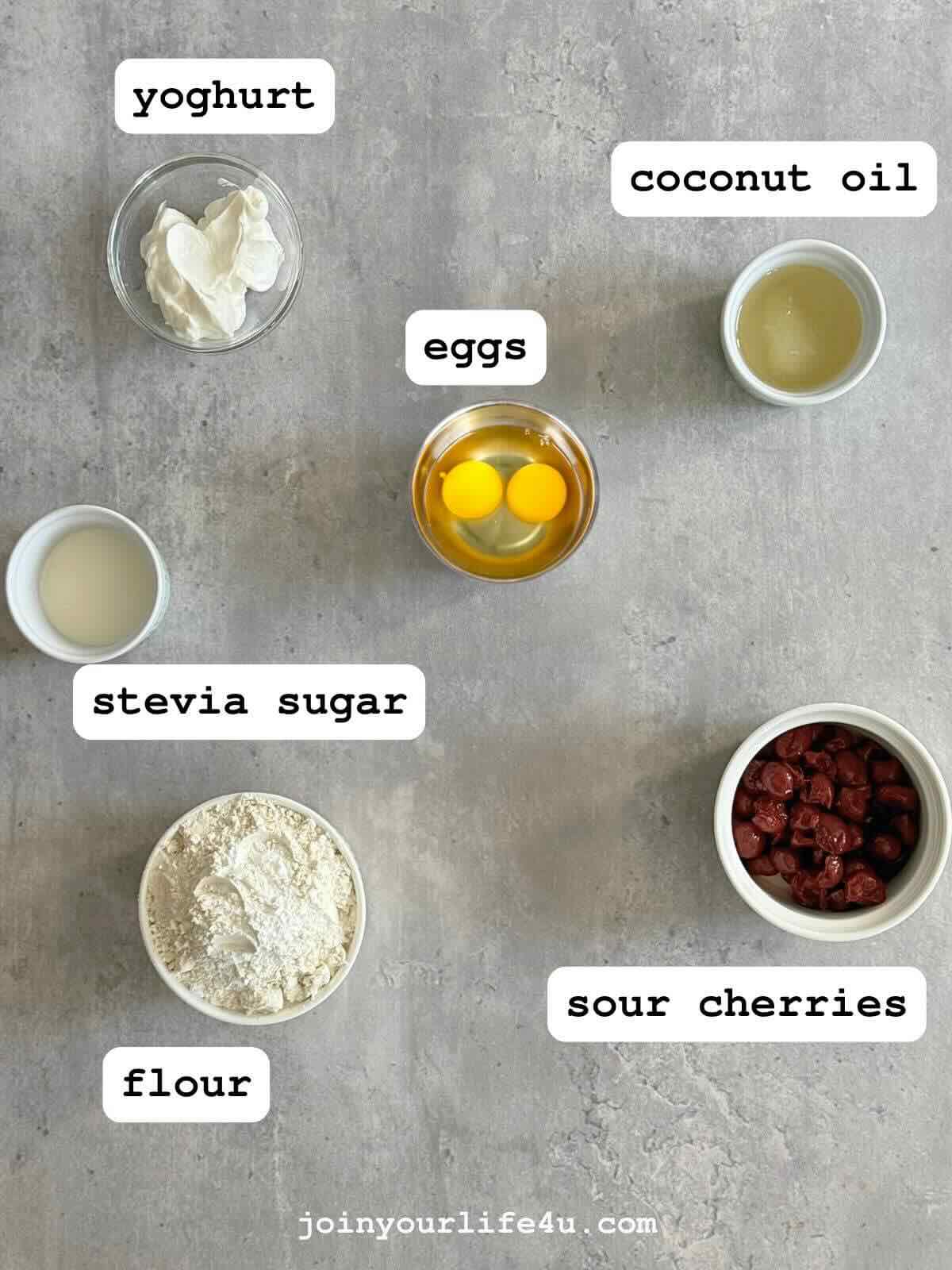 Two eggs, coconut oil, yoghurt, stevia sugar, self-rising flour, and sour cherries on a table.