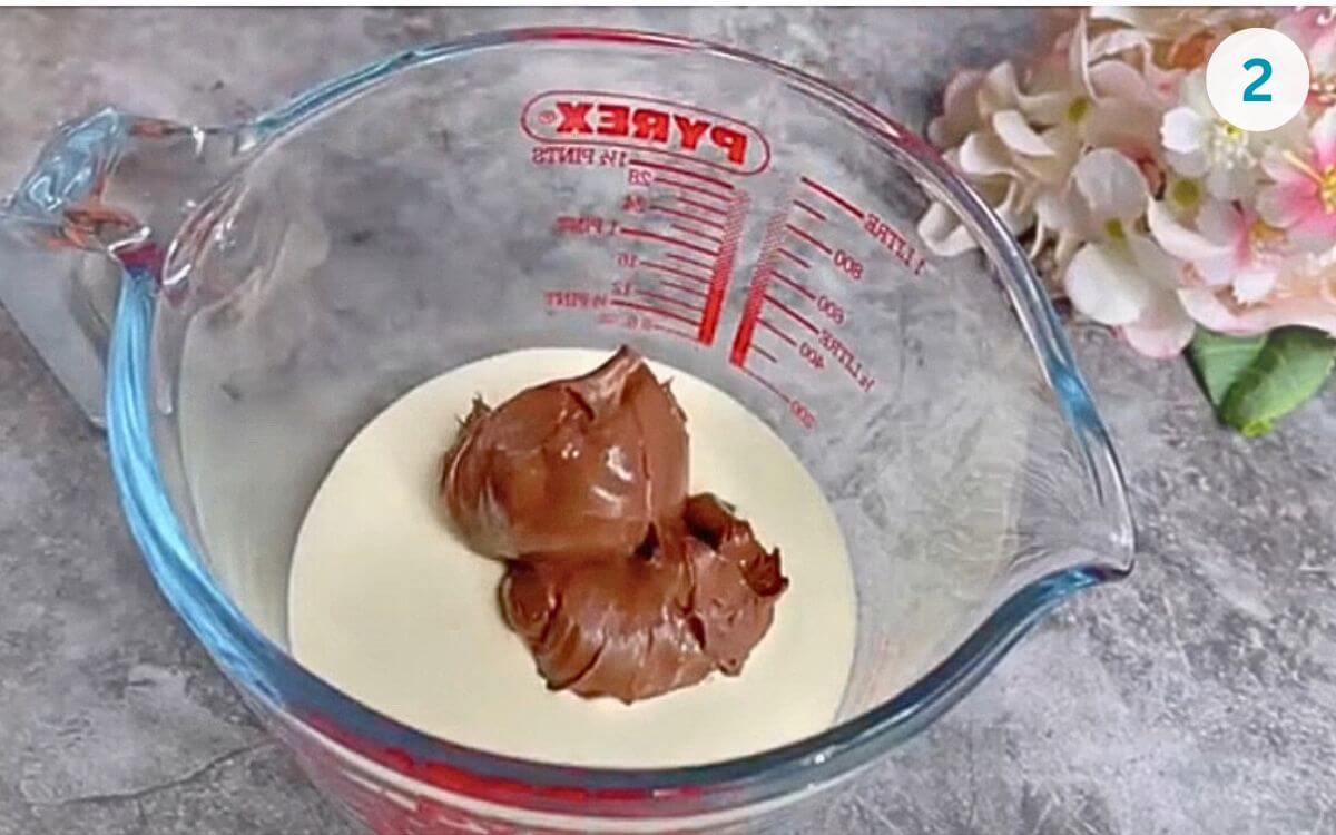 Nutella added to the cream in a glass bowl, ready to be microwaved.