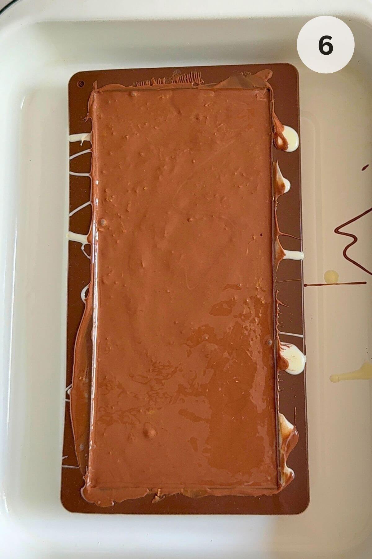 Chocolate poured over pistachio filling, spread with a brush, ready to freeze. 