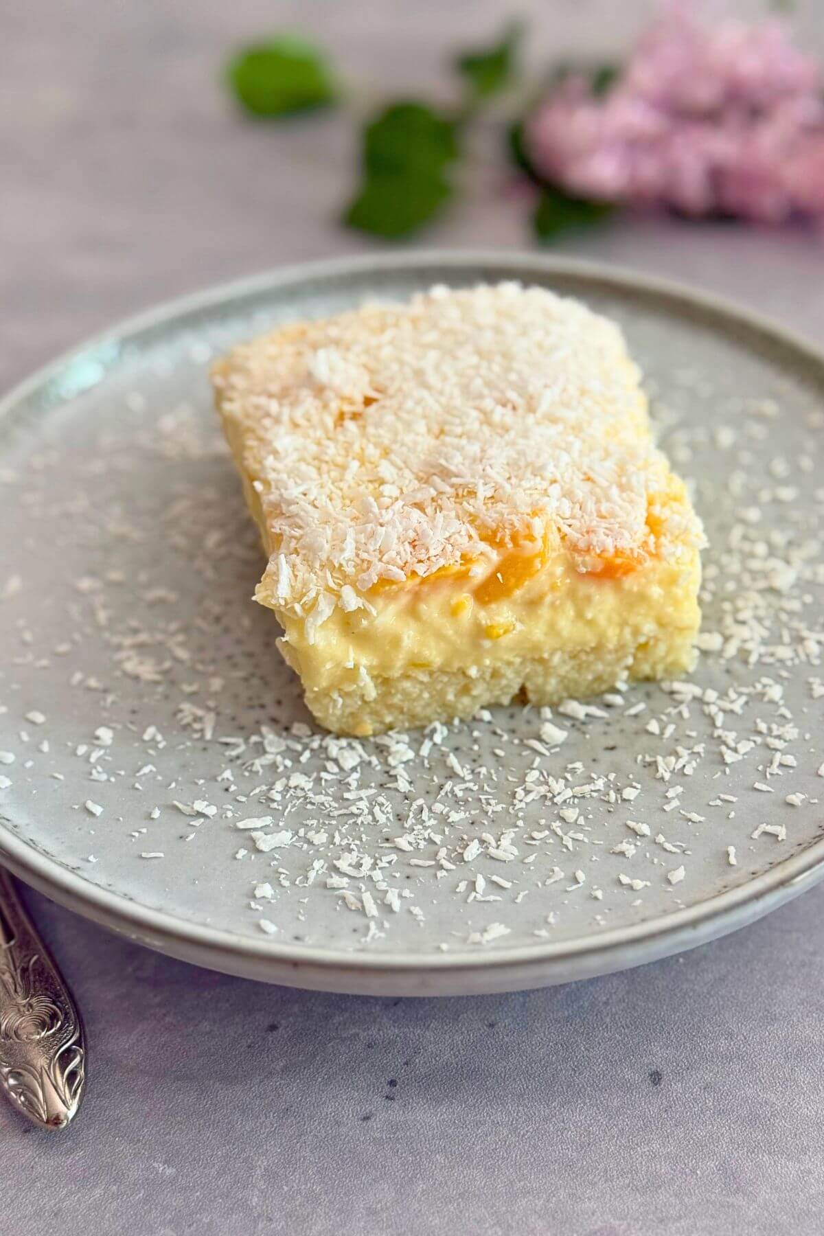 Close-up of creamy peach vanilla cake slice with grated white chocolate and peach garnish on a white plate