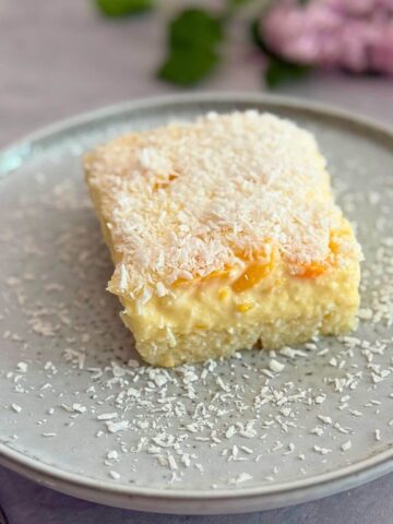 Close-up of creamy peach vanilla cake slice with grated white chocolate and peach garnish on a white plate