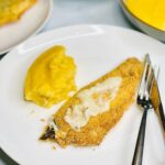 Crispy cornmeal crust fried fish with creamy polenta and garlic butter sauce on a white plate.