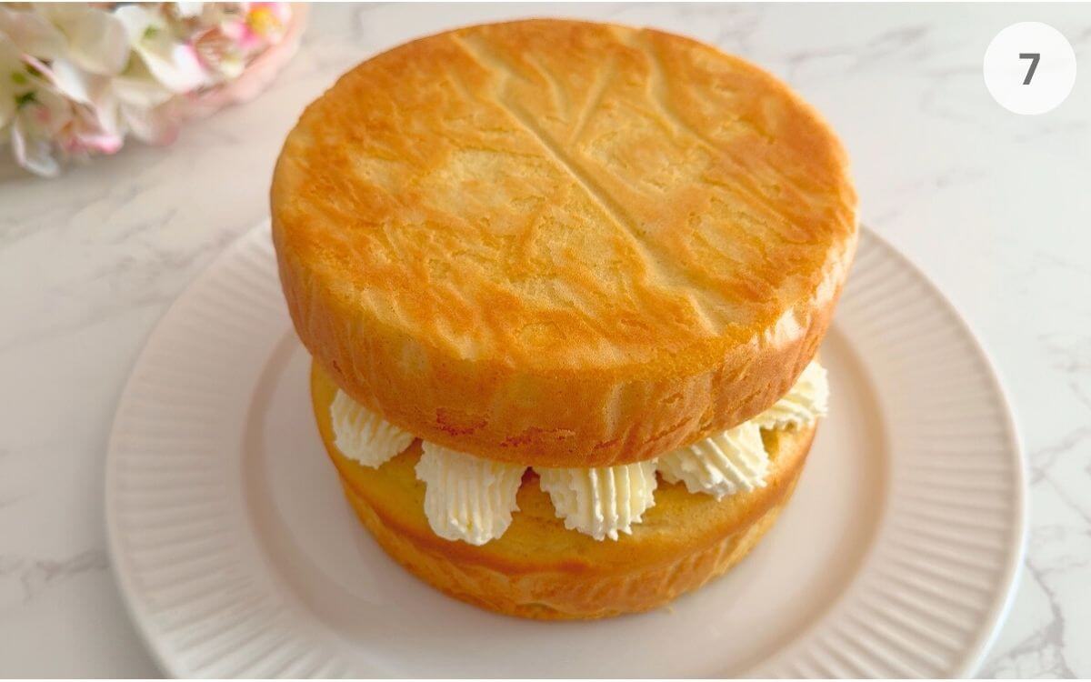 Second sponge layer added, topped with whipped cream and halved strawberries for decoration.