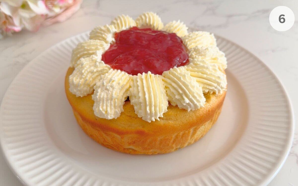 First sponge layer on a plate, brushed with syrup, piped with whipped cream, and filled with jam in the center.