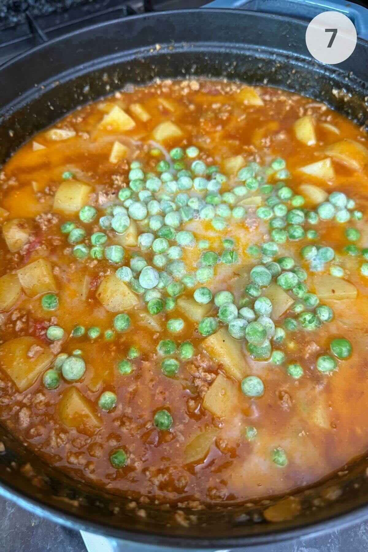 Coconut milk, zucchini, and peas simmering in the pan, forming a creamy curry sauce.
