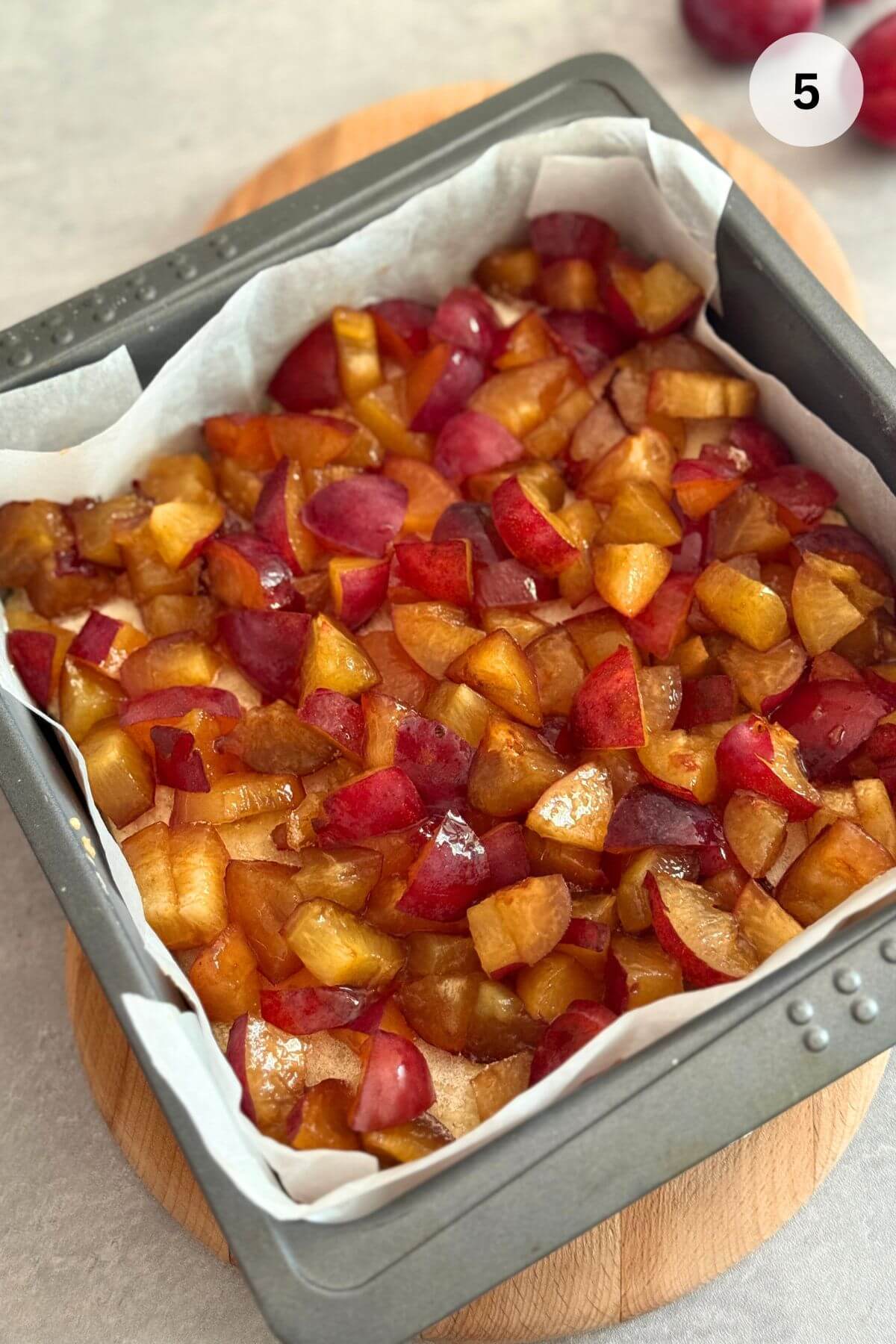 A pre-baked base in a pan topped with neatly arranged, quartered purple plums.