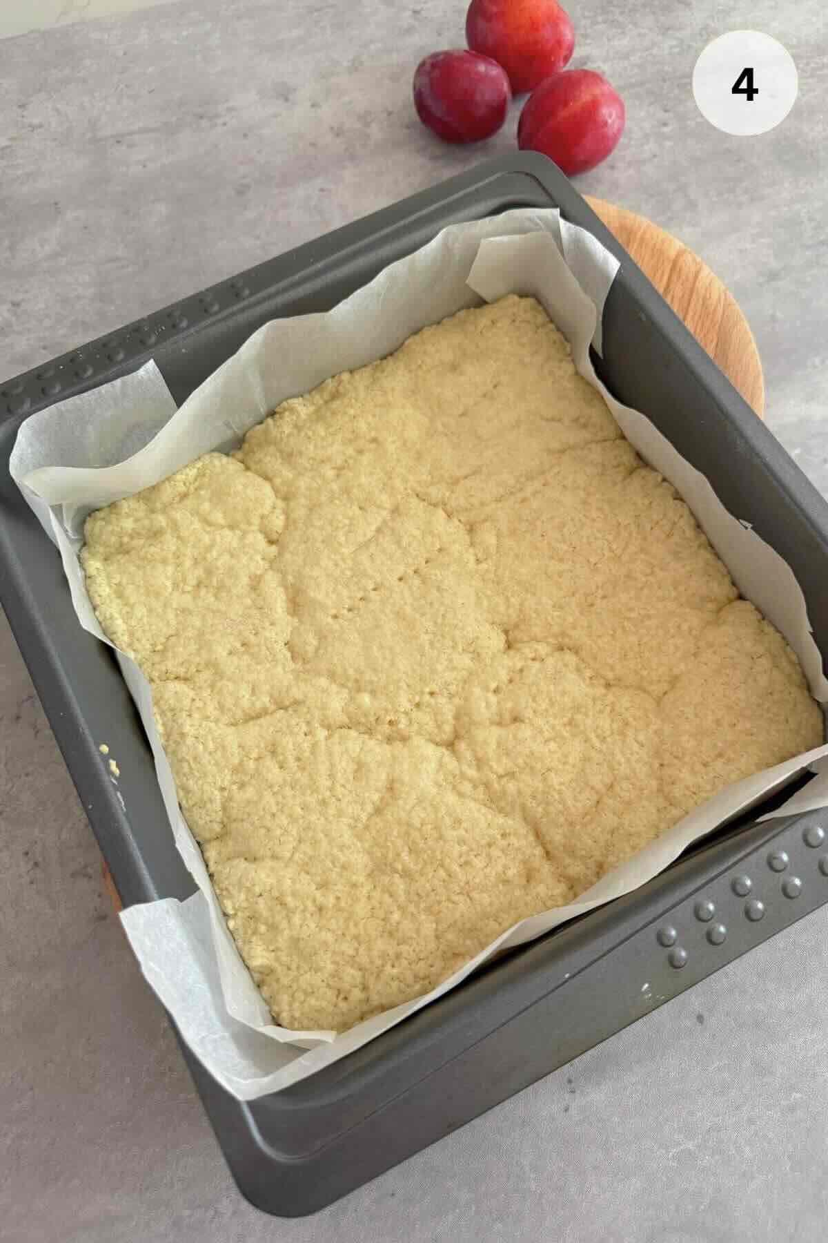 A square baking pan holding a golden, partially baked dough base, resting on a counter.