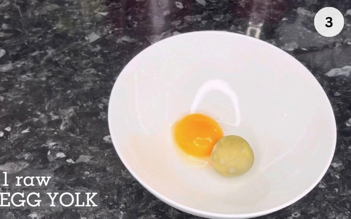 Egg yolks being mashed with lemon juice and salt in a bowl.
