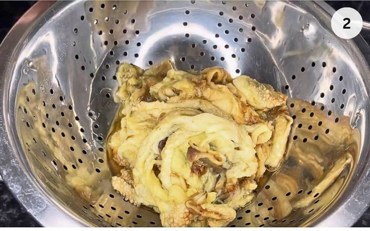 Charred eggplant flesh draining in a colander after peeling off the blackened skin.
