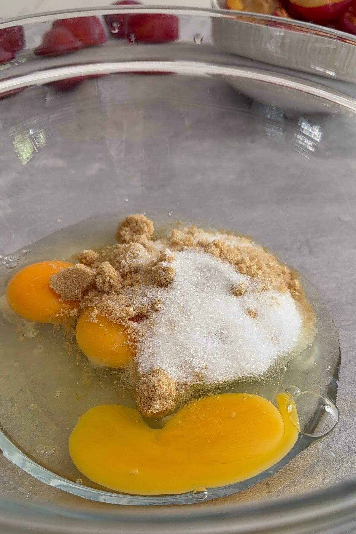 Whole eggs and granulated sugar measured in a glass bowl, ready to be whisked for a homemade plum cake.